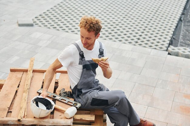 Een pauze nemen Jonge man die overdag in uniform aan het werk is in de bouw