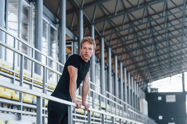 Een pauze nemen Sportieve jonge kerel in zwart shirt en broek overdag buiten