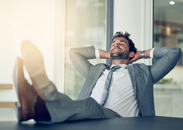 Foto een pauze nemen van zaken shot van een zakenman die achterover leunt in zijn stoel met zijn voeten op een bureau en handen achter zijn hoofd