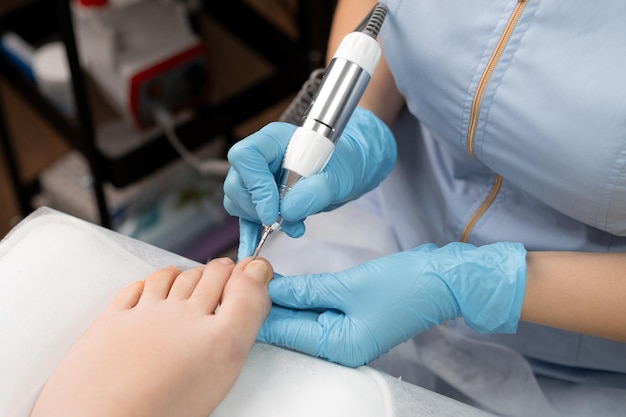 Een pedicure-expert in rubberen handschoenen voert een hardware-pedicure uit voor vrouwen met behulp van een spijkerboor