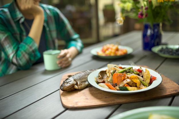 Een persoon die buiten aan een tafel zit Een gekookte verse vis en een gerecht van groenten