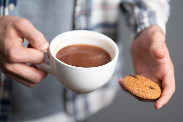 Een persoon die een kop warme chocolademelk en een zoet koekje vasthoudt