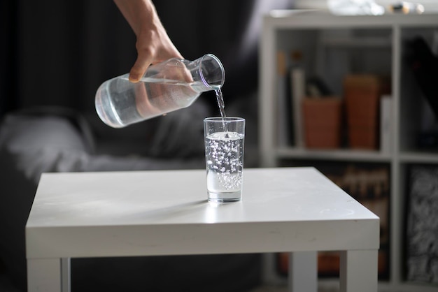 Een persoon houdt een fles vast en giet water in het glas
