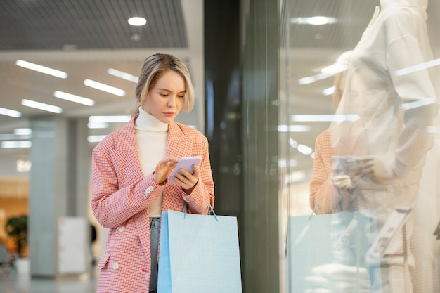 Een persoon in een roze jas met een blauwe tas en smartphone