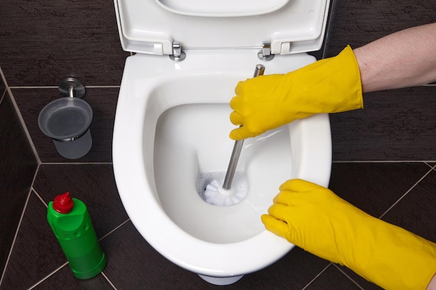 Een persoon in gele rubberen handschoenen maakt de toiletpot schoon met een borstel en een ontsmettingsmiddel