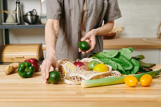 Een persoon in vrijetijdskleding die vegetarisch ontbijt bereidt aan de keukentafel