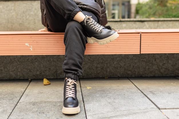 Een persoon met zwarte sneakers zit op een bank met het woord op de zijkant.