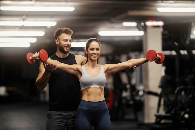 Een persoonlijke trainer helpt een sportvrouw met dumbbells oefeningen in een sportschool