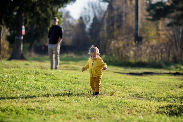 Een peuter-peuter in een geel jasje rende weg van zijn vader in een herfstpark, nazomer.