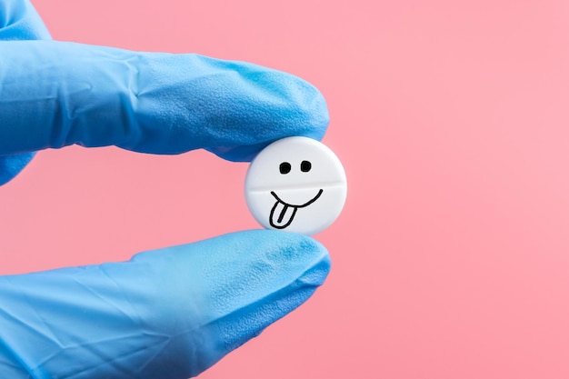 Een pil met een emoticon in een hand in een medische handschoen op een roze achtergrond Gezondheidsbehandeling en preventie