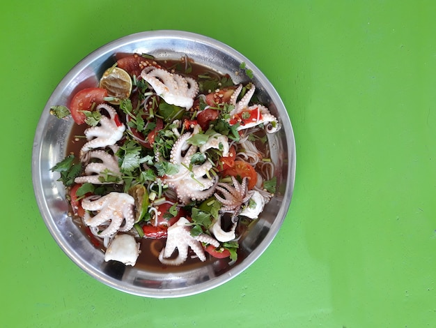 Een plaat van pittige squid salade met lokale noedels op de groene achtergrond