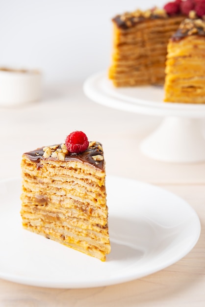 Een plak van zelfgemaakte pannenkoekcake met chocoladekaramel walnoten en framboos op een witte plaat