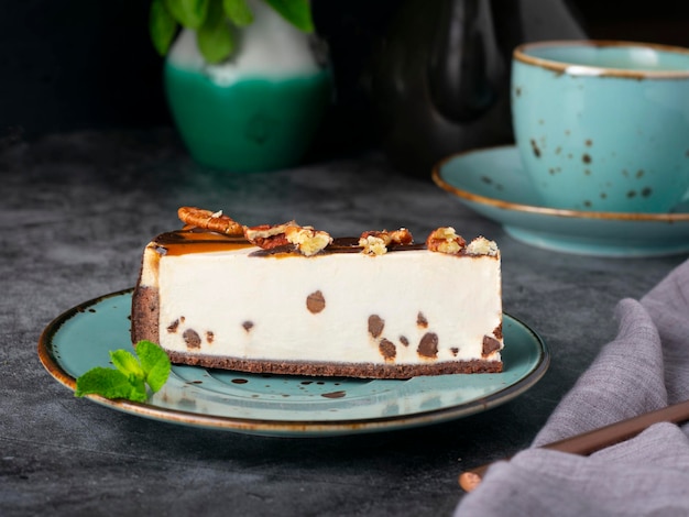 Een plakje cheesecake met chocoladeschilfers met munt, theekopje