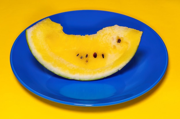 Foto een plakje zoete, verse gele watermeloen geserveerd op een blauwe schaal tegen een kleurrijke achtergrond