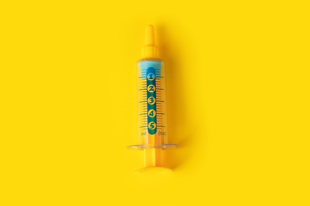 Foto een plastic miniatuurstuk speelgoed spuit over gele achtergrond, geneeskunde en vaccinconcept