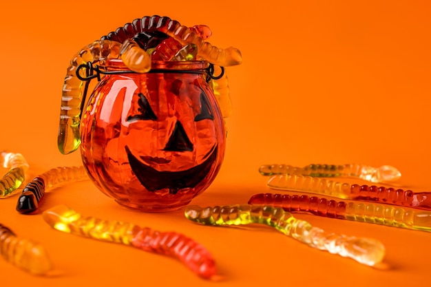 Een pompoenvormige pot is gevuld met marmeladewormen op een oranje achtergrondconcept Hallowee