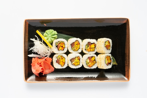 Een portie maki sushi met een assortiment van Japanse bijgerechten in een rechthoekige keramische plaat op een witte achtergrond