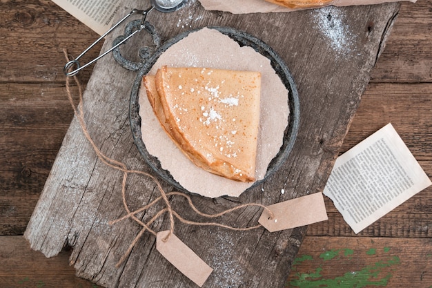 Een portie pannenkoeken wordt opgerold en op houten planken bestrooid met poedersuiker.