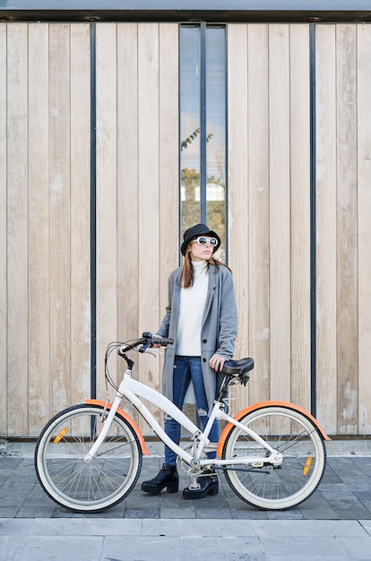 Een portret jonge mooie blanke meisje, gekleed in een grijs jasje, een witte trui en een hoed met een fietstocht in de stad