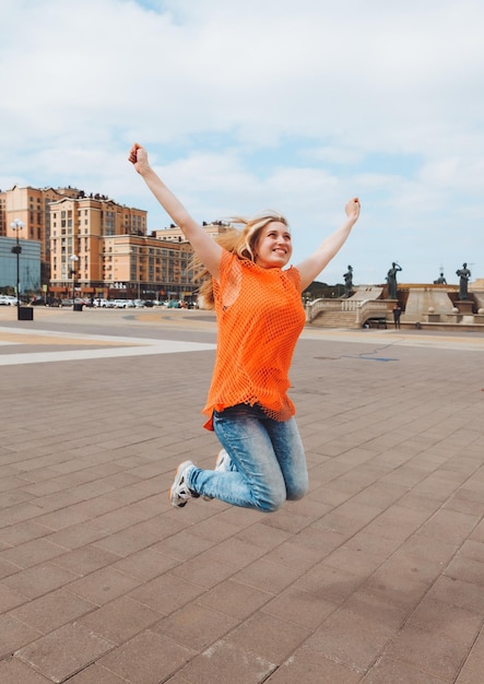 Een portret op ware grootte van een vrolijk positief meisje dat in de lucht springt met haar handen omhoog tegen de achtergrond van de stadsgeneratie z