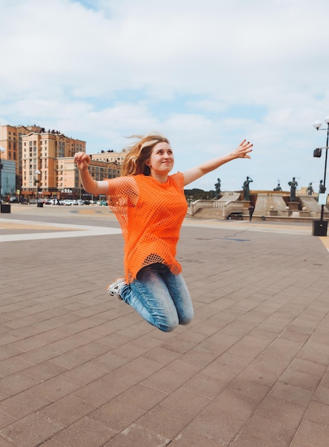 Een portret op ware grootte van een vrolijk positief meisje dat in de lucht springt met haar handen omhoog tegen de achtergrond van de stadsgeneratie z