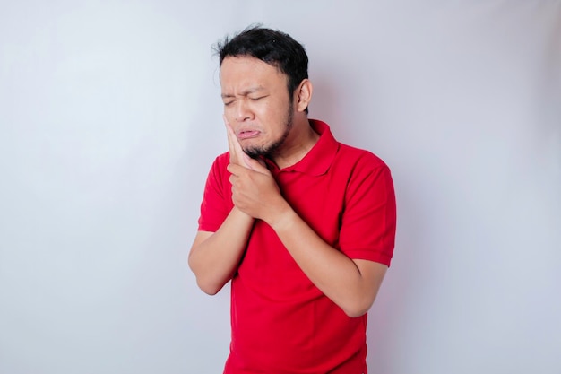 Een portret van een Aziatische man met een rood t-shirt geïsoleerd door een witte achtergrond ziet er depressief uit