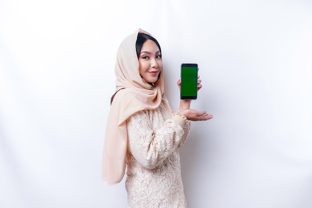 Een portret van een gelukkige Aziatische moslimvrouw die een hijab draagt en haar telefoonscherm toont geïsoleerd door een witte achtergrond