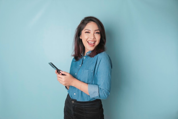 Een portret van een gelukkige Aziatische vrouw lacht en houdt haar smartphone vast in een blauw shirt geïsoleerd door een blauwe achtergrond