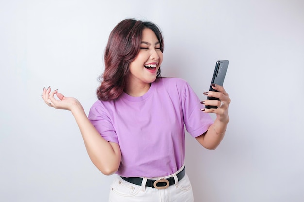 Een portret van een gelukkige Aziatische vrouw lacht en houdt haar smartphone vast met een lila paarse tshirt geïsoleerd door een witte achtergrond