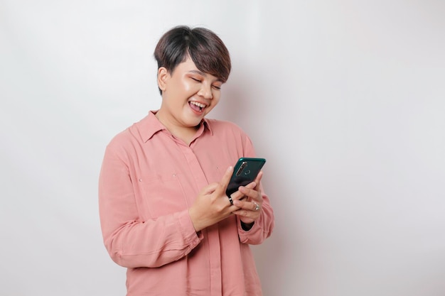 Een portret van een gelukkige Aziatische vrouw lacht en houdt haar smartphone vast met een roze shirt geïsoleerd door een witte achtergrond