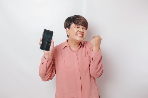 Een portret van een gelukkige Aziatische vrouw lacht en toont kopieerruimte op haar smartphone met een roze shirt geïsoleerd door een witte achtergrond