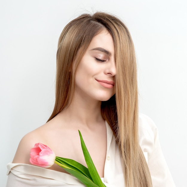 Een portret van een gelukkige jonge blanke vrouw met gesloten ogen en een roze tulp tegen een witte achtergrond met kopie ruimte