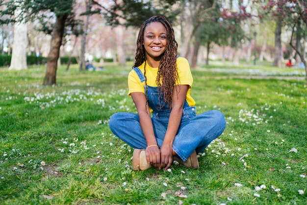 Een portret van een jonge Afrikaanse vrouw die op het gras in een park zit en glimlacht
