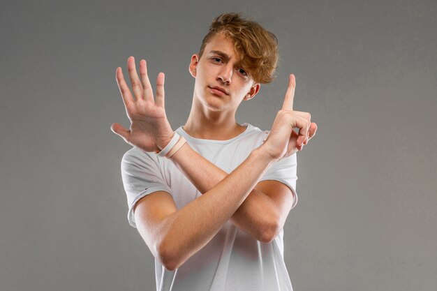 Een portret van een jonge blanke man met kort rood krullend haar in een wit t-shirt toont zes vingers geïsoleerd op een grijze achtergrond