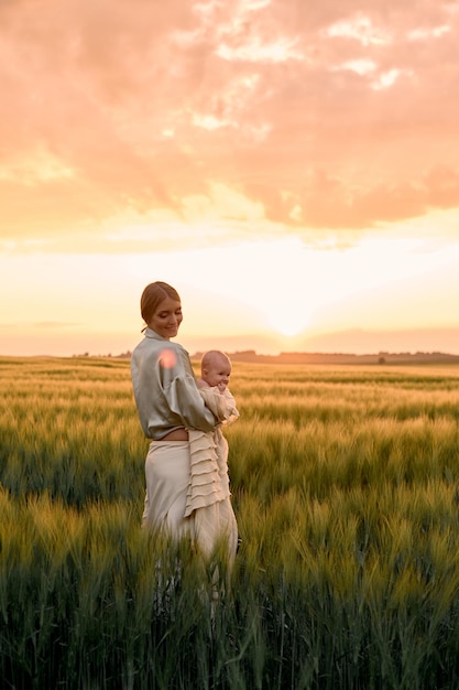 Een portret van een jonge moeder met een baby in haar armen bij zonsondergang in het veld happy family concept