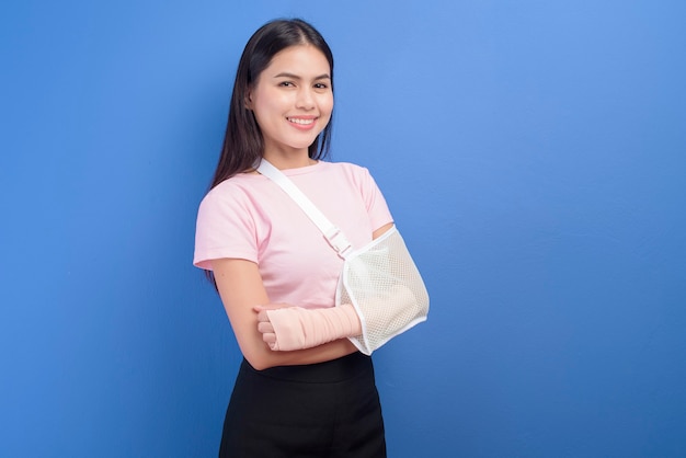 Een portret van een jonge vrouw met een gewonde arm in een mitella over blauwe muur