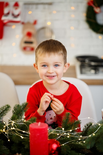 Een portret van een jongen die in de keuken zit aan de kersttafel, die is versierd voor het nieuwe jaar. Kerstdecoratie in de keuken