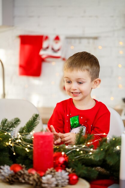 Een portret van een jongen die in de keuken zit aan de kersttafel, die is versierd voor het nieuwe jaar. Kerstdecoratie in de keuken