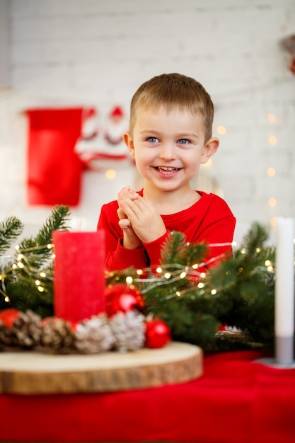 Een portret van een jongen die in de keuken zit aan de kersttafel, die is versierd voor het nieuwe jaar. Kerstdecoratie in de keuken