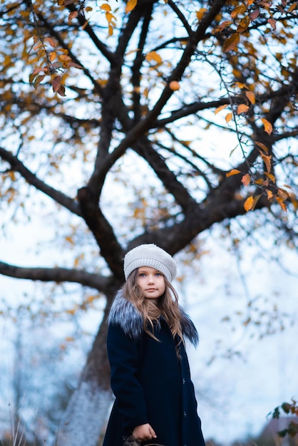 Een portret van een meisje met een grijze hoed en een donkerblauwe jas in de herfst in het park