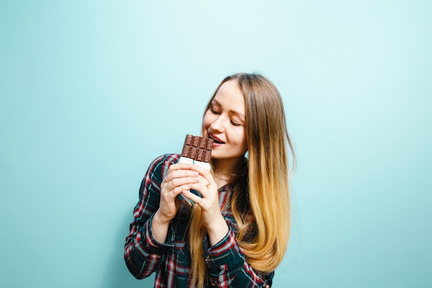 Een portret van een mooi blond meisje dat chocolade eet, is opgewonden op een blauwe achtergrond