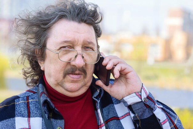 Een portret van een oudere man met een bril die over een mobiele telefoon praat op straat in het park