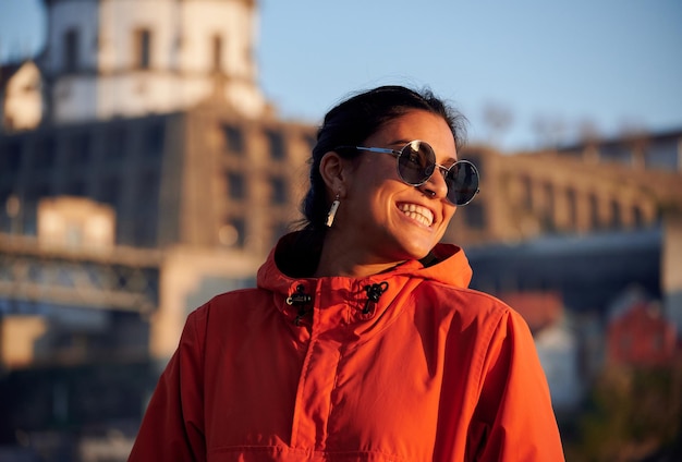 Een portret van een vrolijke jonge vrouw uit Spanje met een zonnebril en een fleurig jasje buiten