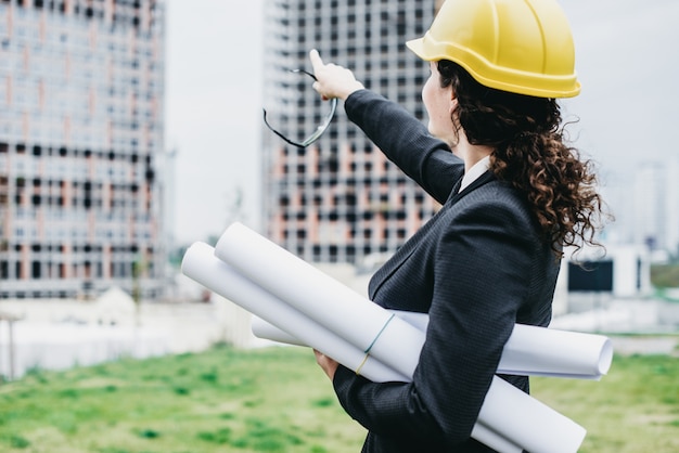 Een portret van ingenieur vrouw die naar de bouw kijkt. Vrouw architect met blauwdruk in de hand en gele helm met selecte focus. Concept Engineer en bedrijfswerk.