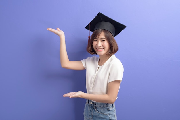 Een portret van jonge Aziatische student die afstuderen GLB over studioachtergrond draagt.