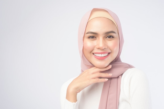 Een portret van jonge glimlachende moslimvrouw die een roze hijab over witte studio als achtergrond draagt.