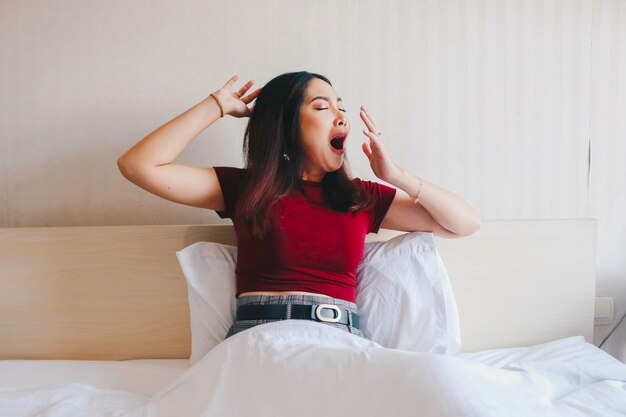 Een portret van slaperige jonge Aziatische vrouw die op bed geeuwt