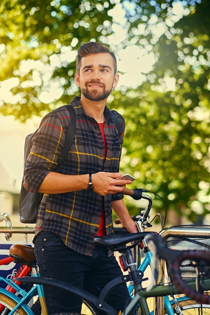 Een positief bebaarde man gekleed in een fleece shirt met behulp van een smartphone in de buurt van fietsenstalling.