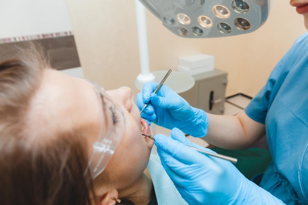 Een positieve donkerharige vrouw zit in het kantoor van de tandarts tijdens een controle tandarts die de tanden van de vrouw onderzoekt