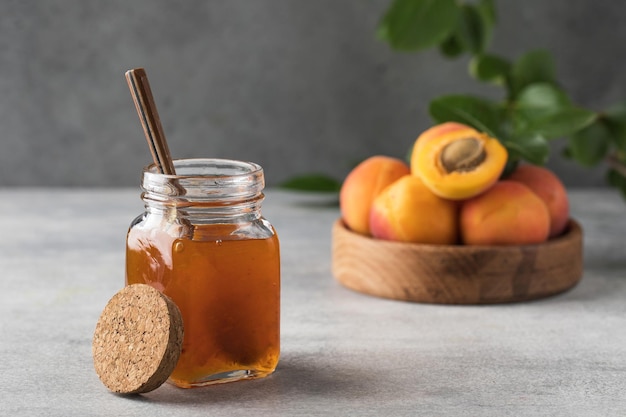 Een pot met abrikozenjam en een lepelclose-up op een grijs fruitbehoud